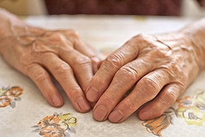 aging hands resting on a table cloth with flowers on it. 