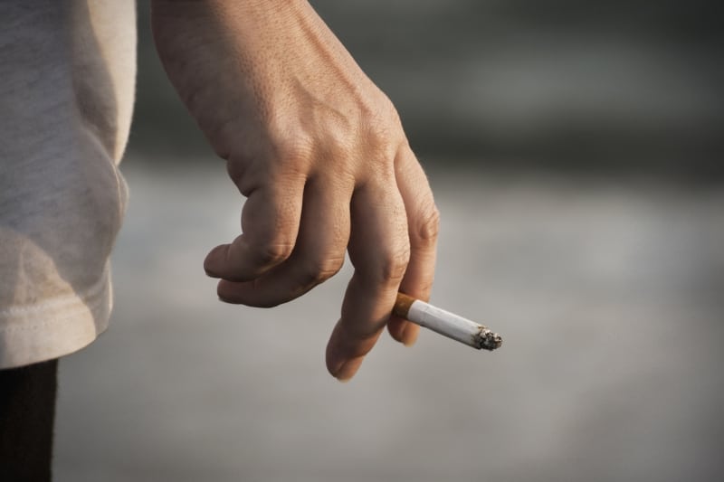 male's hand holding smoldering cigarette