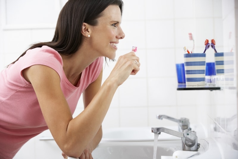 woman brushing her teeth in front of mirror 