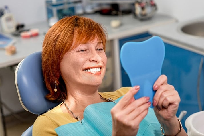 mature woman looking in a hand held mirror, seeing her new smile