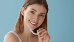 woman holding up clear aligners next to her smile